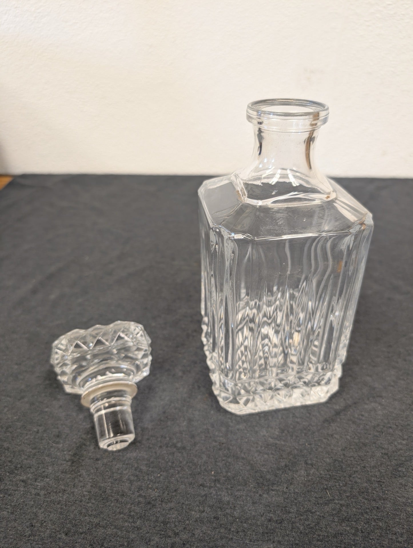 Square clear glass liquor decanter with its stopper sitting beside it.