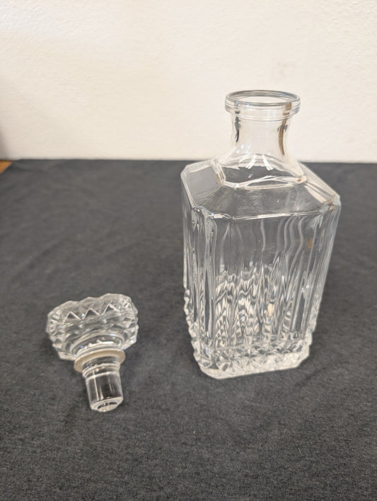 Square clear glass liquor decanter with its stopper sitting beside it.