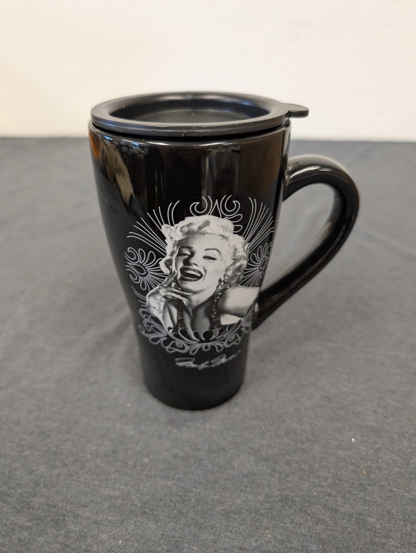Black ceramic travel mug with a lid featuring Marilyn Monroe.