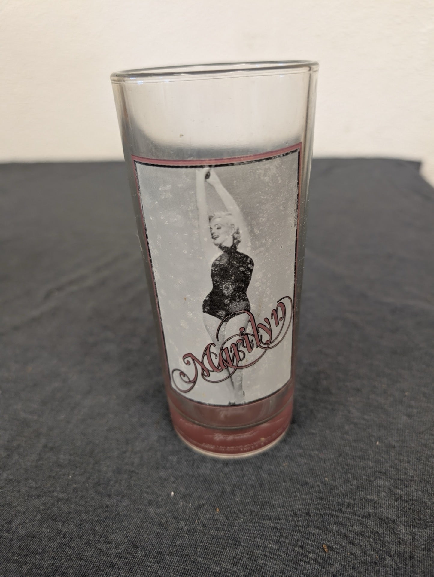 Vintage clear drinking glass featuring Marilyn Monroe in a black bodysuit with pink script
