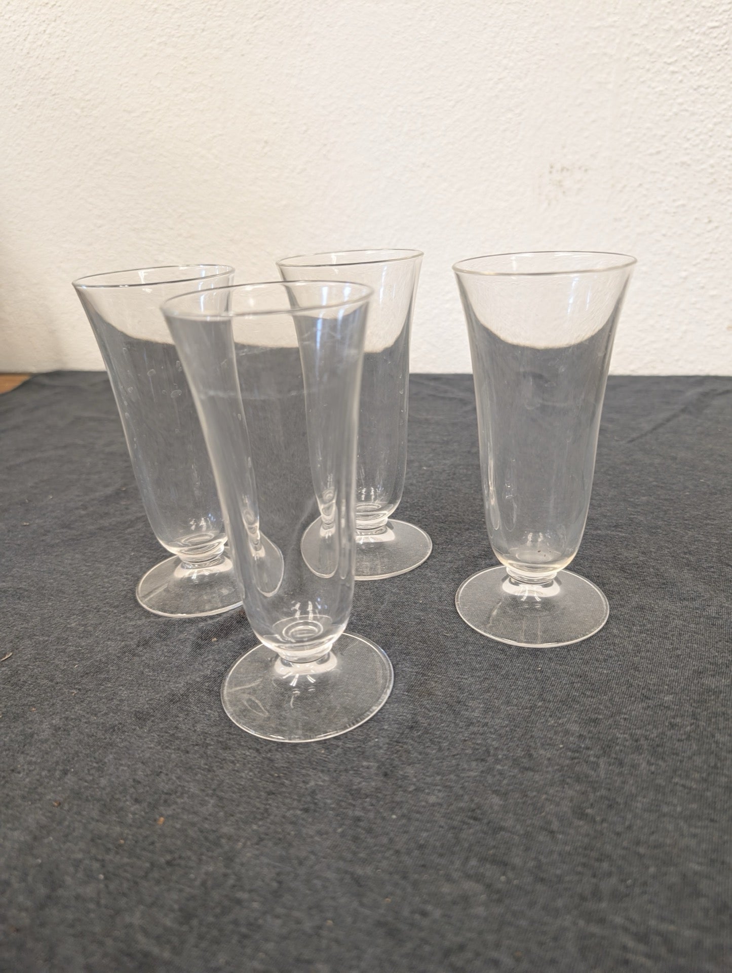 Four matching clear footed glasses arranged on a dark surface