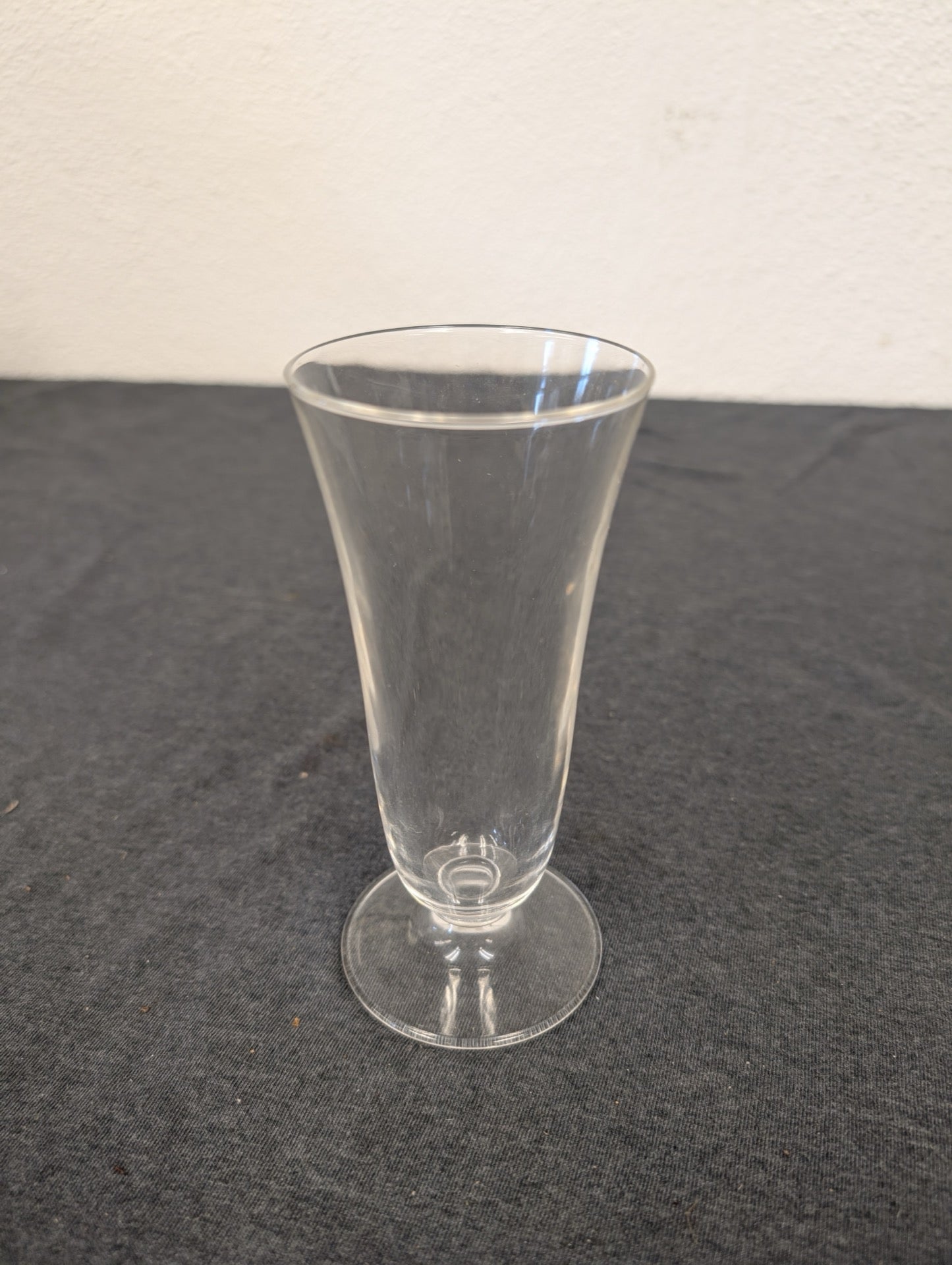 Single clear footed glass standing on a dark surface