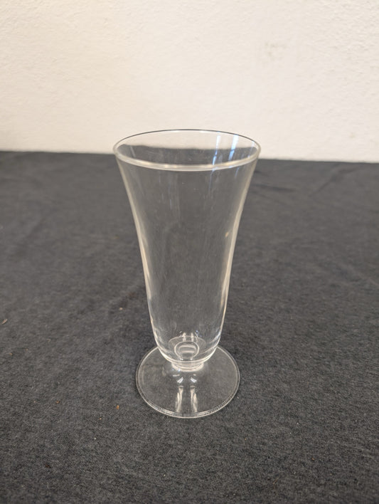Single clear footed glass standing on a dark surface