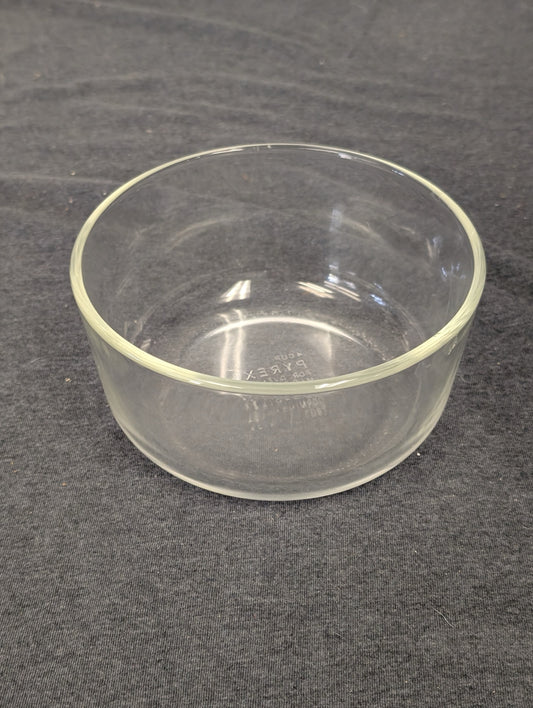 Clear glass round Pyrex bowl sitting on a gray fabric surface.