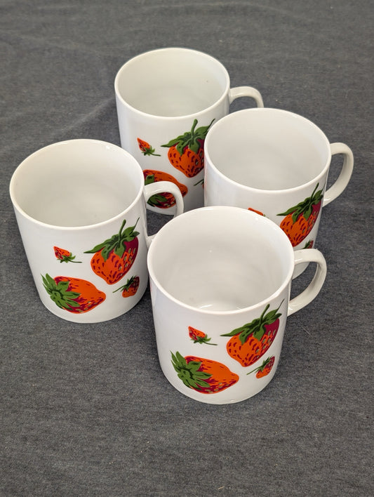Four white ceramic mugs with printed strawberry and green leaf patterns arranged on a gray surface.