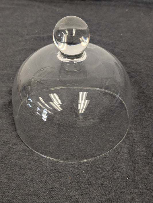 Clear glass cloche dome with a round ball knob on top resting on a gray surface.