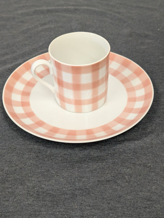 Pink and white gingham checkered teacup resting on a matching saucer.