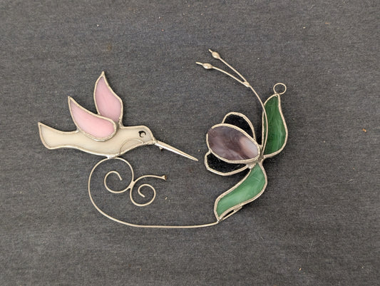 Stained glass art piece depicting a pink and white hummingbird and a purple flower connected by wire.
