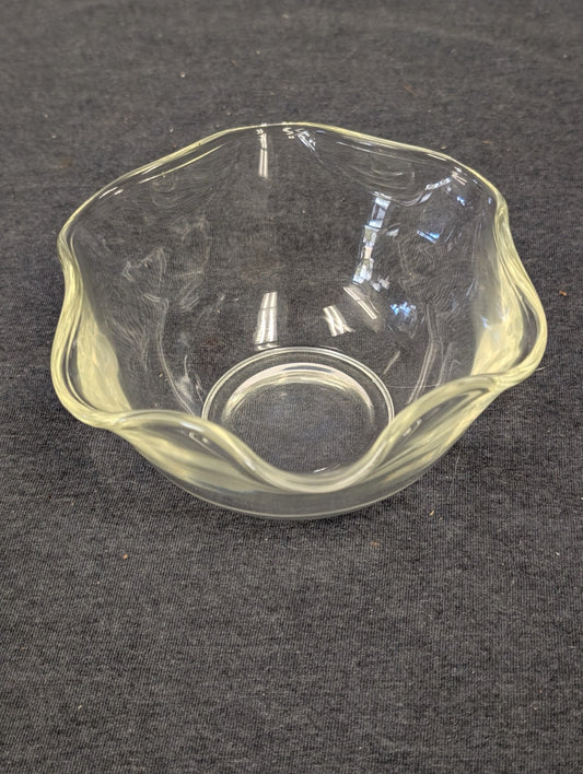 Small clear glass bowl with a scalloped, wavy edge sitting on a dark surface.