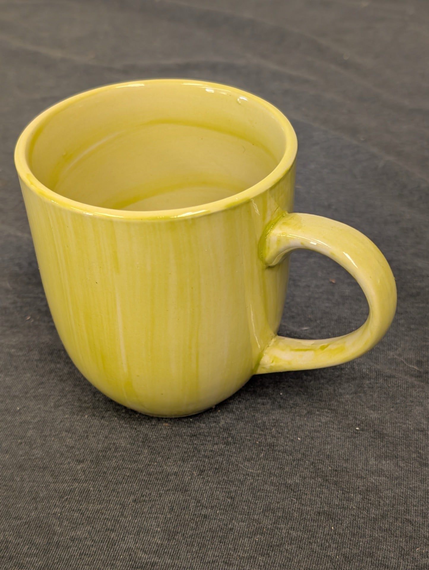 Yellow ceramic coffee mug with a vertical drip glaze effect on a dark background.