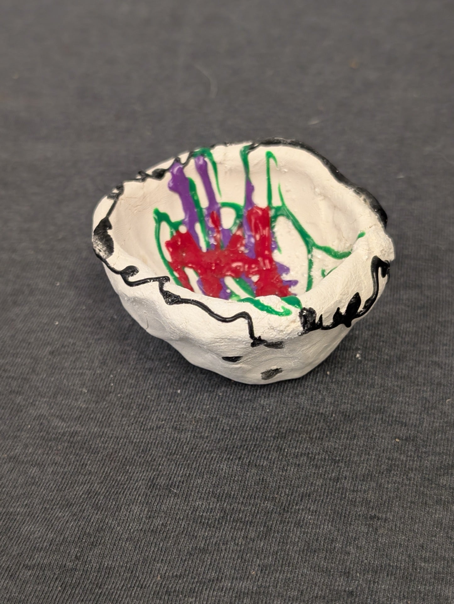 Small handmade white clay bowl with colorful red, green, and purple paint splatters.