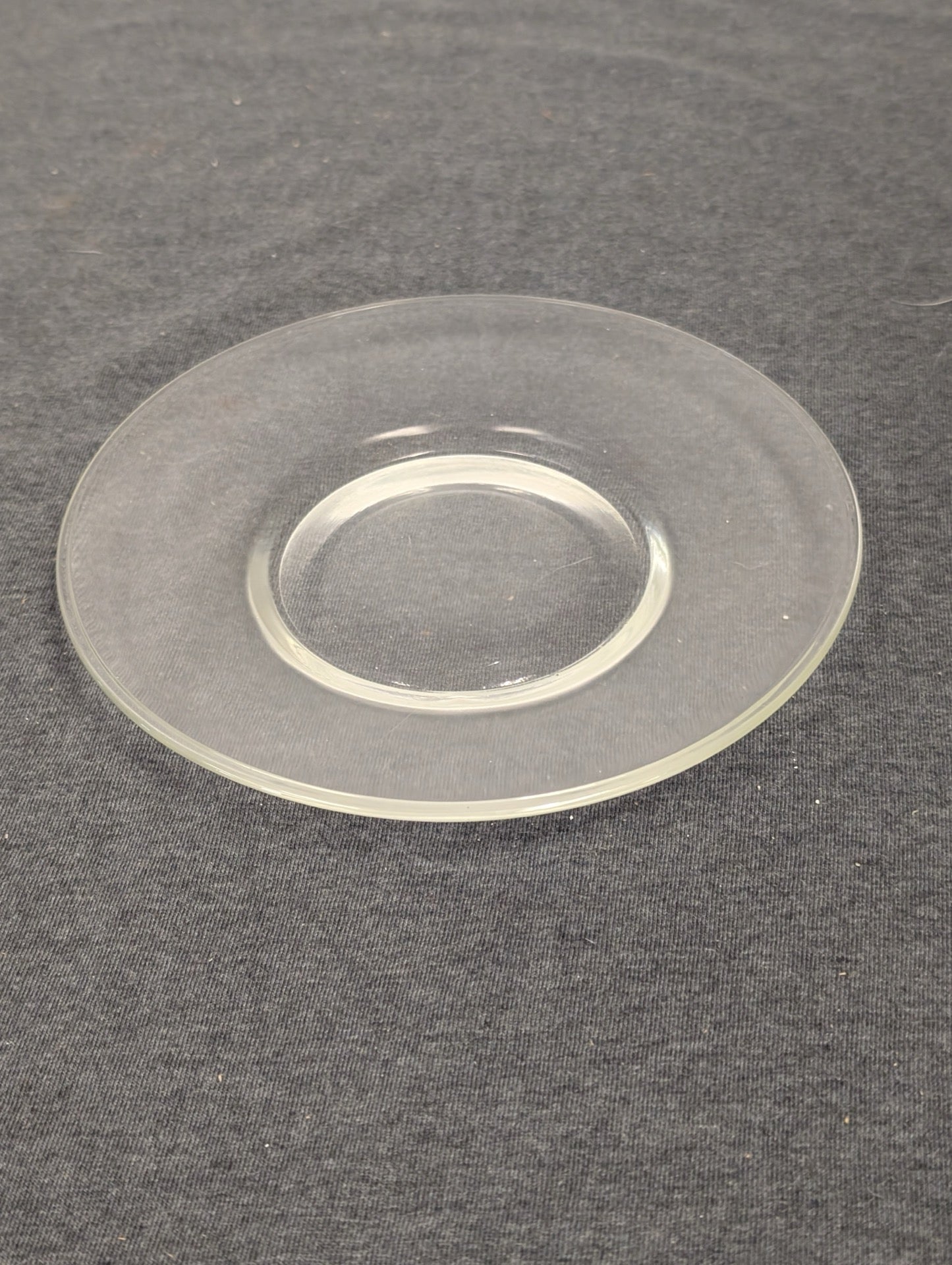 Simple, flat clear glass saucer or small dessert plate on a dark background.