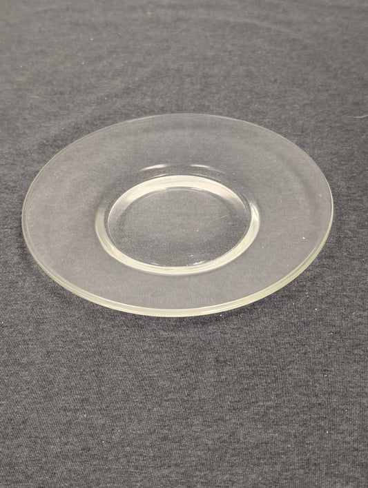 Simple, flat clear glass saucer or small dessert plate on a dark background.