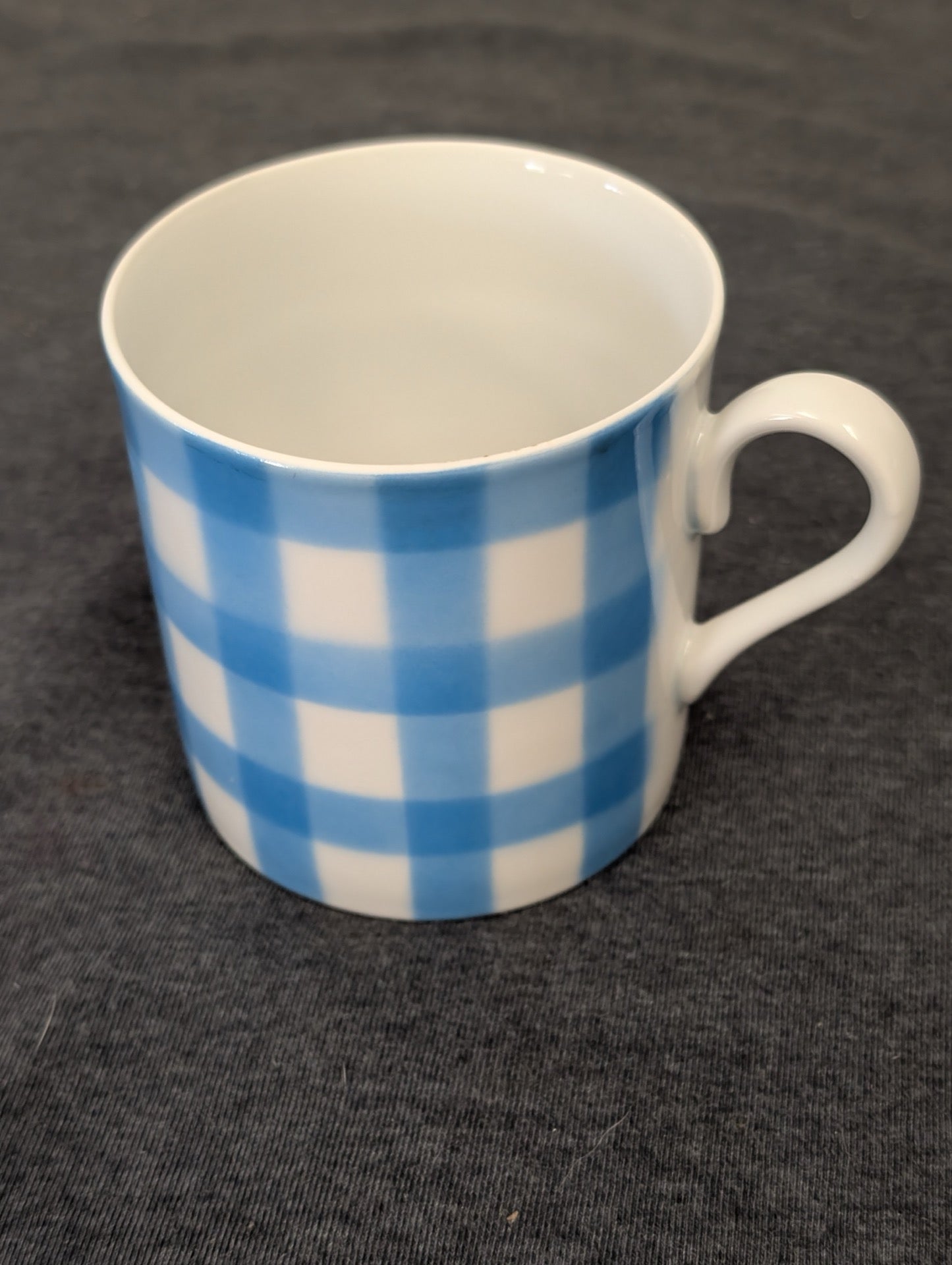 White ceramic coffee mug with a blue gingham checkered pattern on the outside.